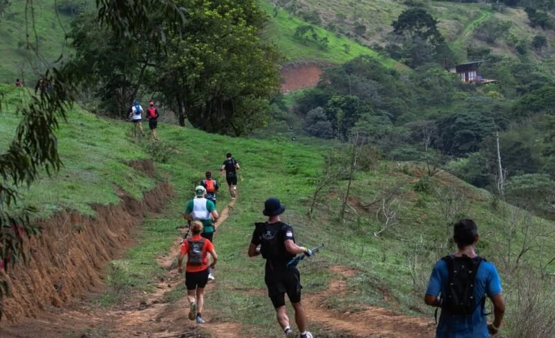Grupo de corredores praticando trail running em trilha verde cercada por vegetação e colinas.
