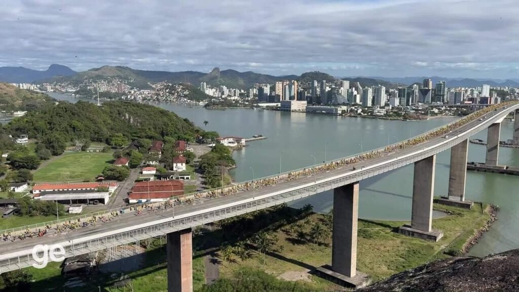 Vista aérea da Terceira Ponte em Vitória com ciclistas e cenário urbano ao fundo.