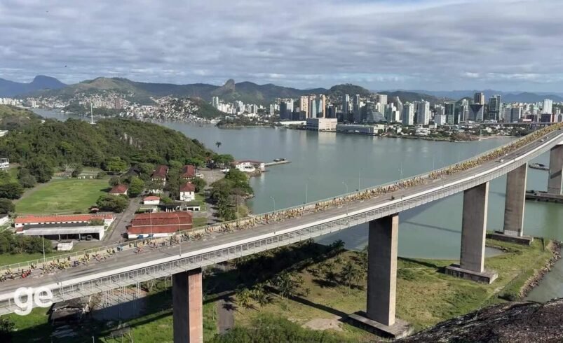 Vista aérea da Terceira Ponte em Vitória com ciclistas e cenário urbano ao fundo.
