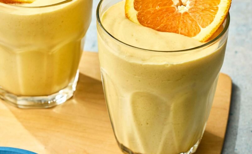 Dois smoothies de laranja decorados com fatias de laranja sobre uma base de madeira.