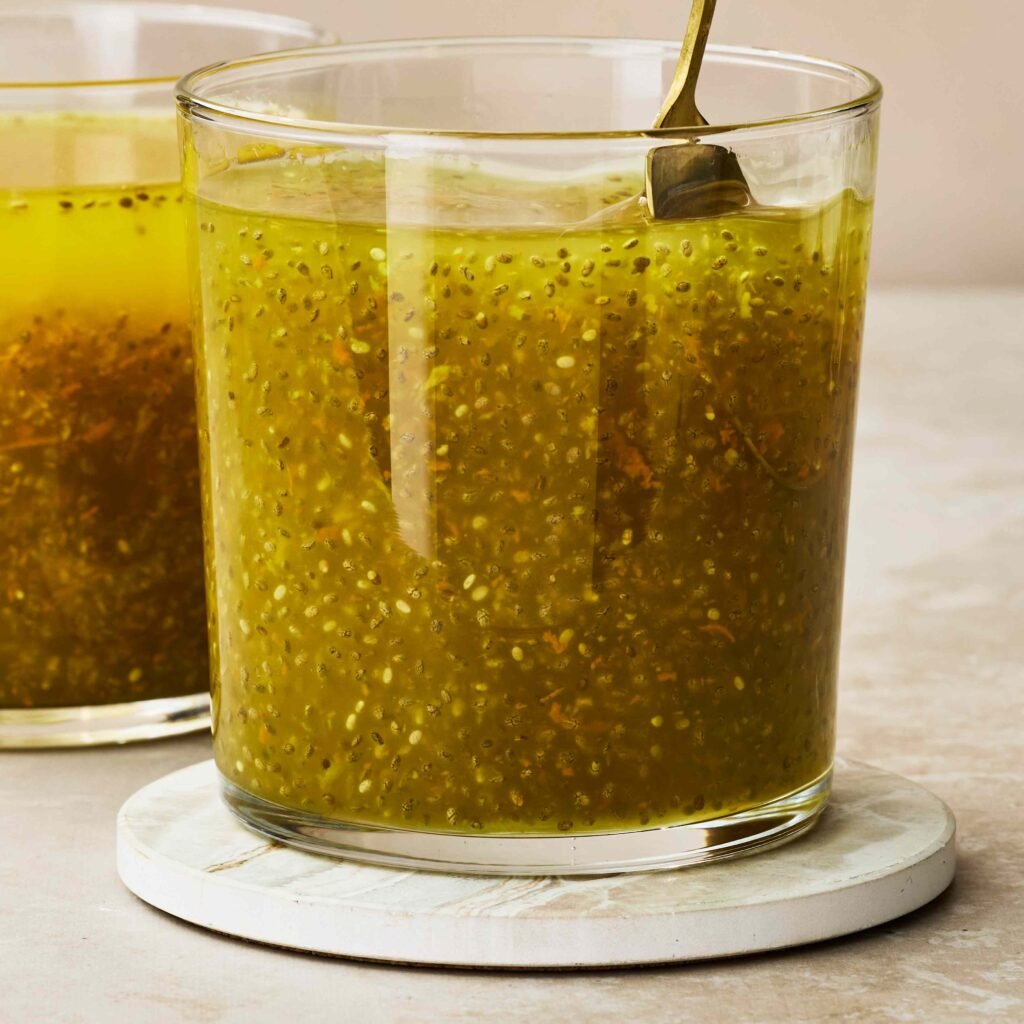 Copo de vidro com bebida amarela e sementes de chia misturadas, em base clara.