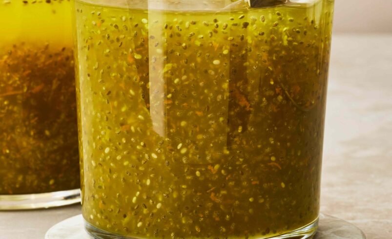 Copo de vidro com bebida amarela e sementes de chia misturadas, em base clara.