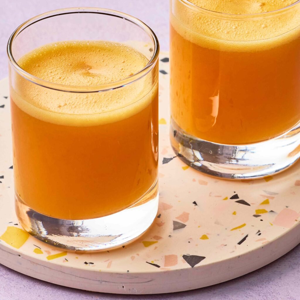 Dois copos de suco de fruta amarelo sobre base clara.