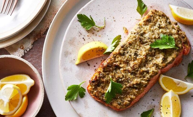 Prato de salmão assado com crosta de ervas acompanhado de fatias de limão.