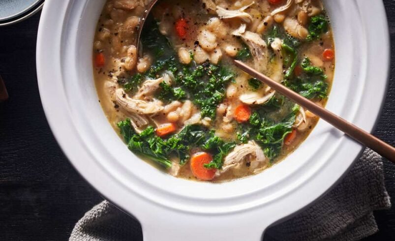 Tigela branca cheia de sopa de frango com cenoura, couve e feijão.