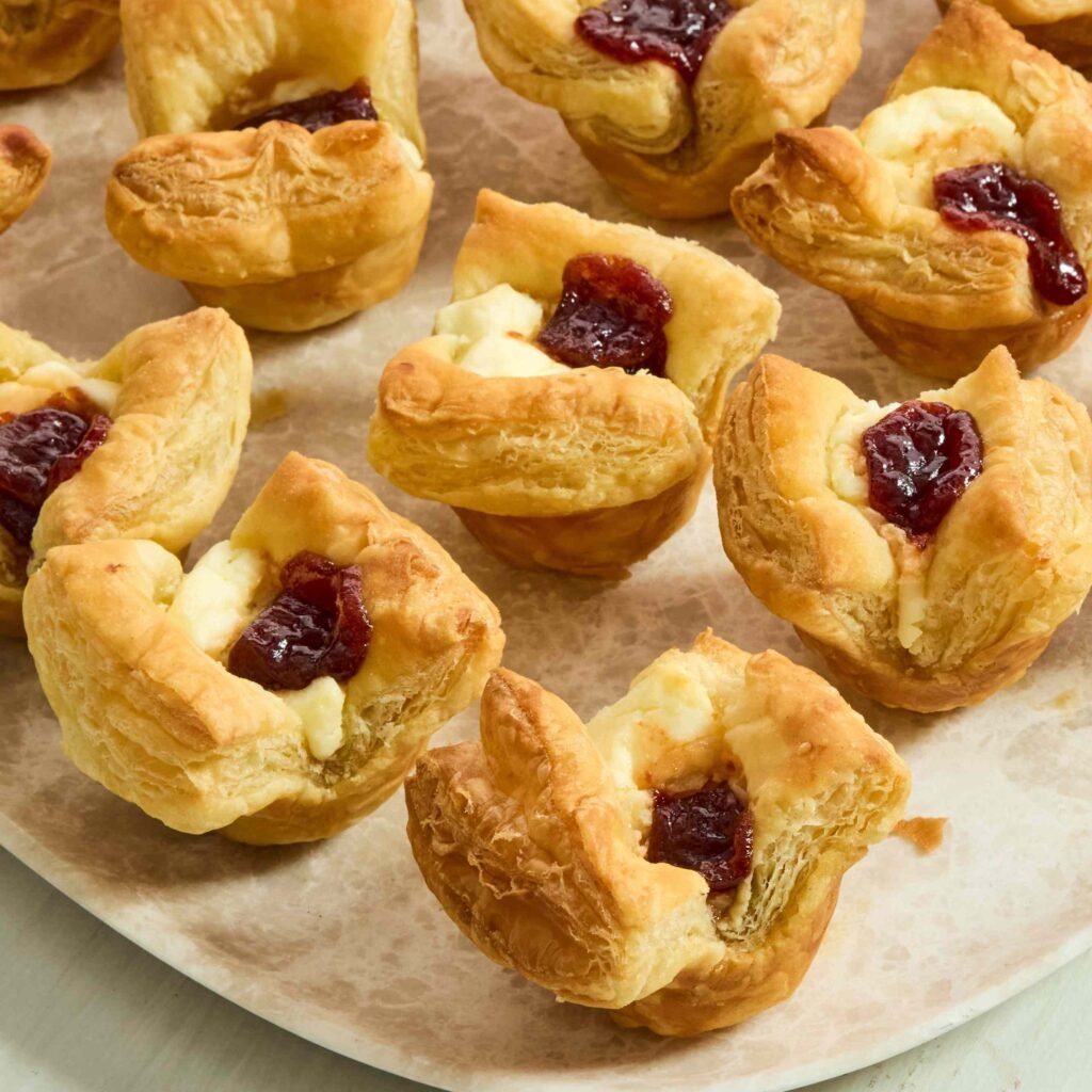 Mais de 10 melhores receitas de aperitivos de Natal 1 Folhados dourados com recheio de creme e geleia sobre prato claro.