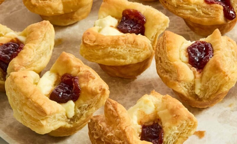 Folhados dourados com recheio de creme e geleia sobre prato claro.