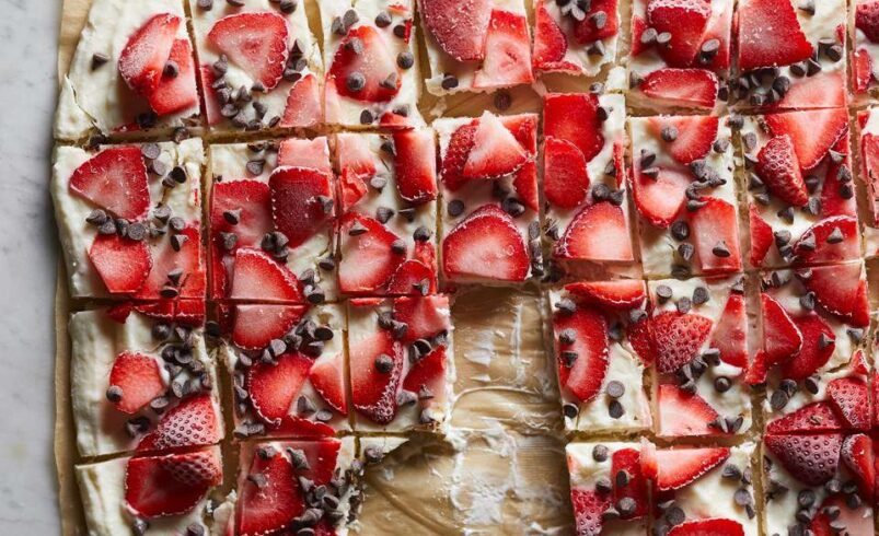 Pedaços de sobremesa gelada com morangos fatiados e gotas de chocolate sobre papel manteiga.