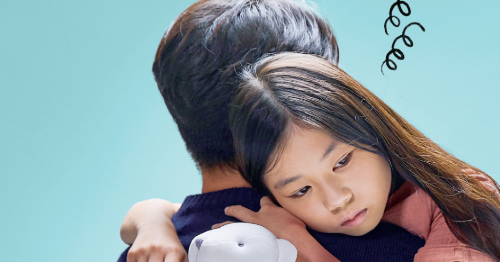 Duas pessoas abraçadas segurando um ursinho branco, fundo azul claro.