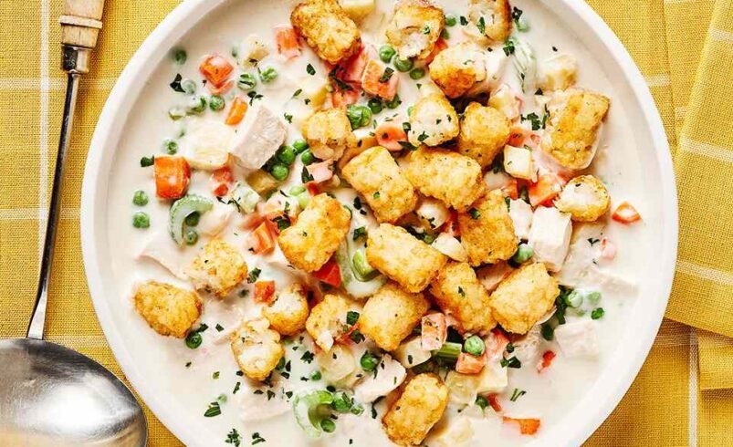 Prato branco com fricassê cremoso, legumes coloridos e batatas douradas.