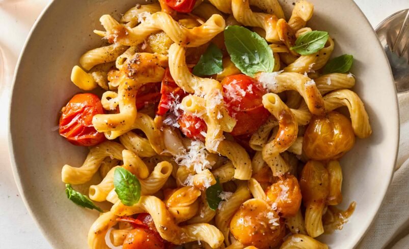 Prato de massa com tomates cereja, folhas de manjericão e queijo ralado.