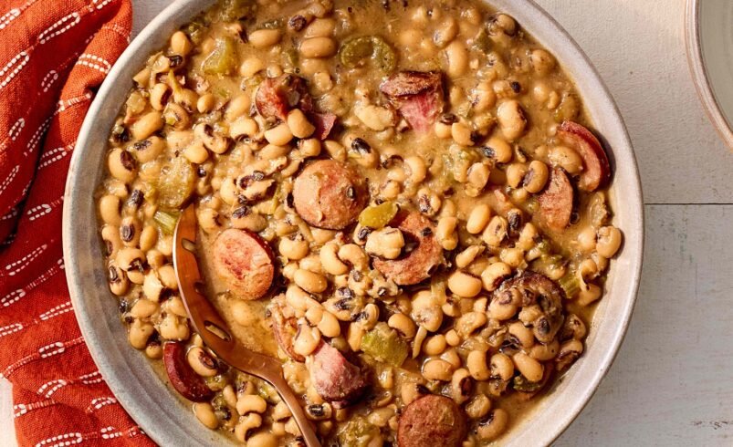 Prato de feijão-fradinho com linguiça defumada e temperos ao lado de guardanapo vermelho.