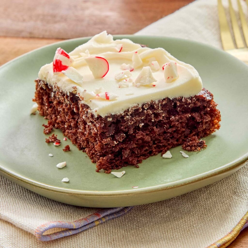 Pedaço de bolo de chocolate com glacê branco e pedacinhos de hortelã em prato verde.