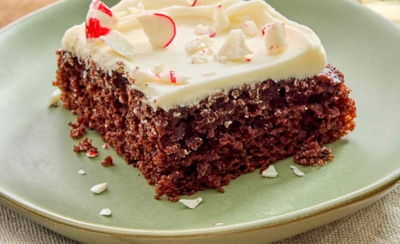 Pedaço de bolo de chocolate com glacê branco e pedacinhos de hortelã em prato verde.