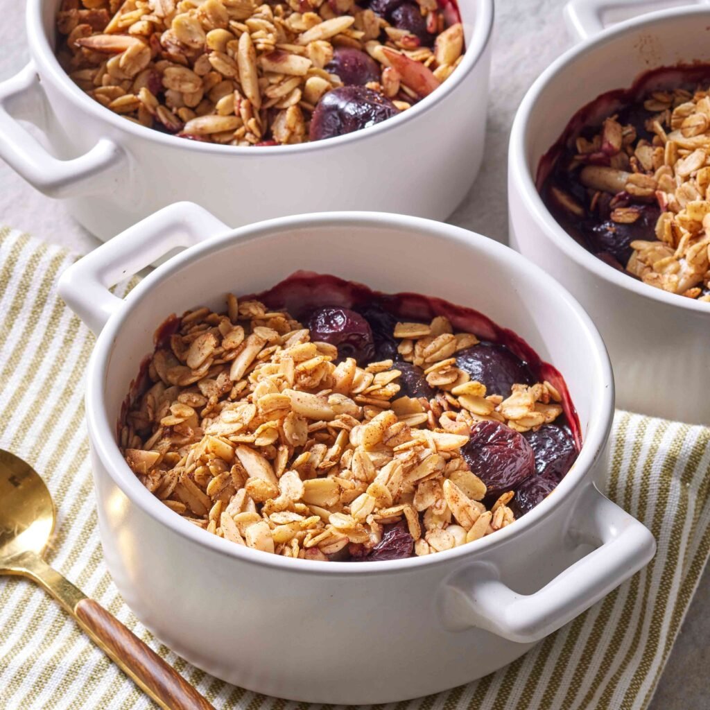 Sobremesa crumble de frutas vermelhas com cobertura de aveia crocante servida em tigelas brancas.