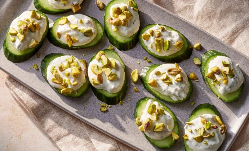 Fatias de avocado com creme e pistache servidas em travessa clara sobre tecido bege.