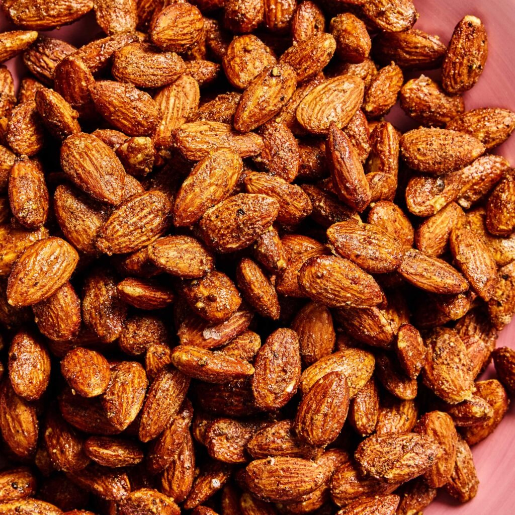 Amêndoas torradas com tempero vistas de perto, em prato rosa.