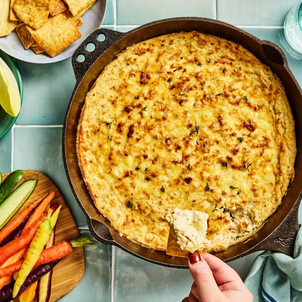 Travessa de queijo gratinado com legumes frescos e biscoitos ao redor.