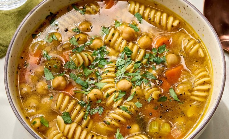 Prato fundo com sopa de grão de bico, macarrão fusilli e ervas frescas.