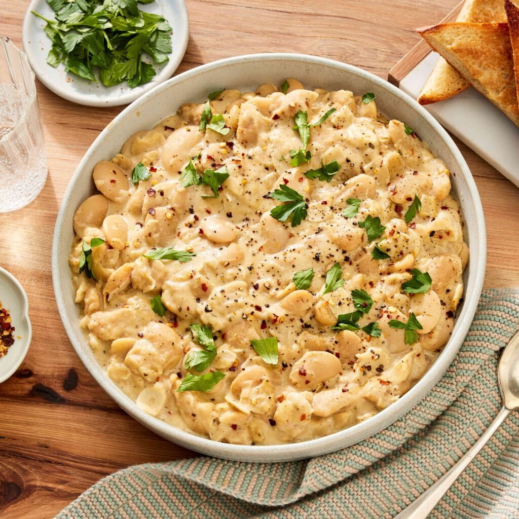 Prato de ensopado cremoso de feijão branco decorado com ervas frescas, servido em uma tigela.