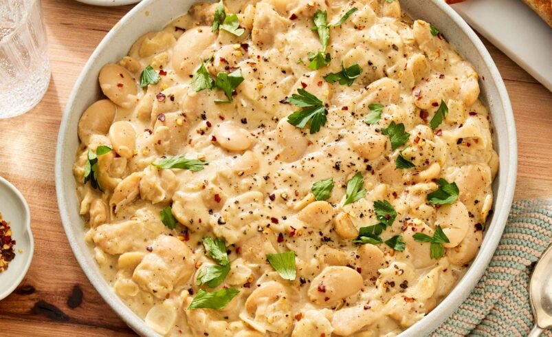 Prato de ensopado cremoso de feijão branco decorado com ervas frescas, servido em uma tigela.