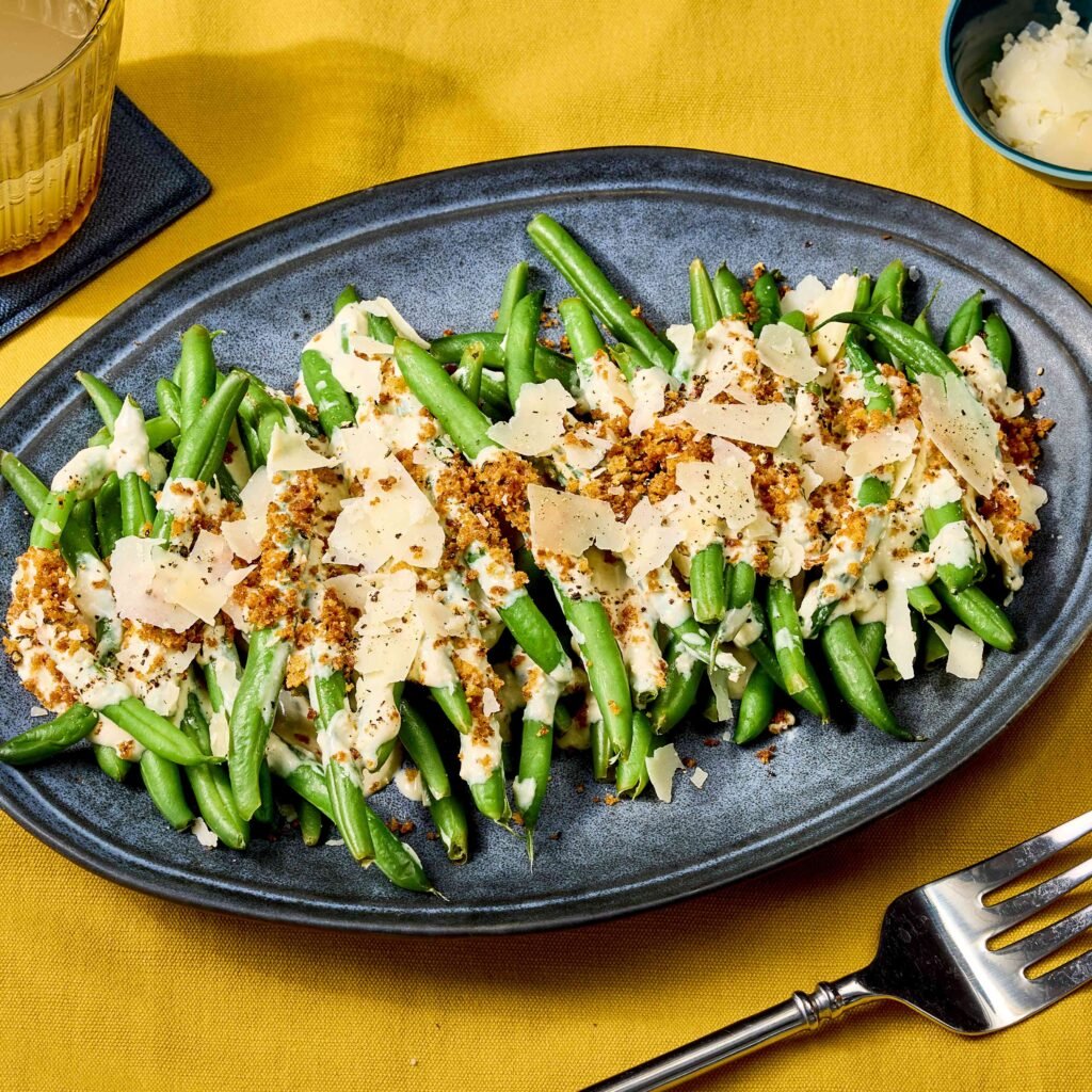 Prato oval com vagem, queijo ralado e cobertura crocante sobre toalha amarela.