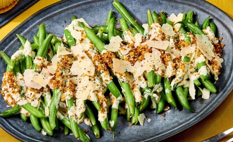 Prato oval com vagem, queijo ralado e cobertura crocante sobre toalha amarela.