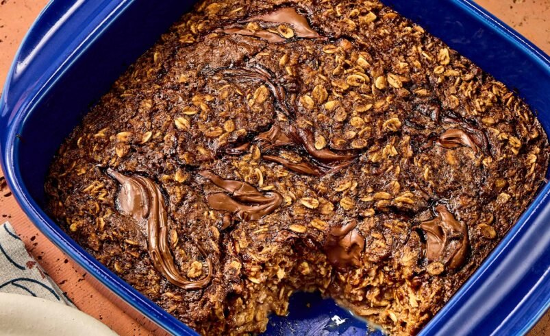 Aveia assada com chocolate em uma travessa azul retangular sobre superfície rústica.