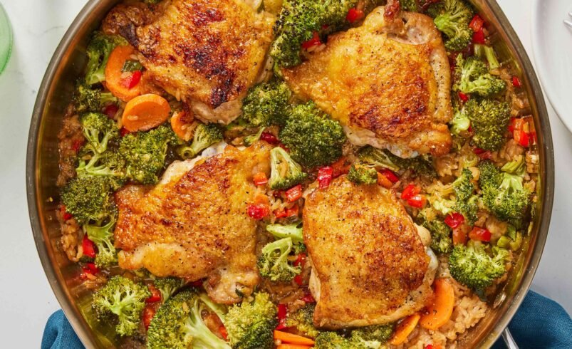 Coxas de frango douradas com brócolis, cenouras e pimentões em uma panela.