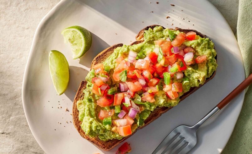 Torrada com avocado, pico de gallo e limão em prato claro.