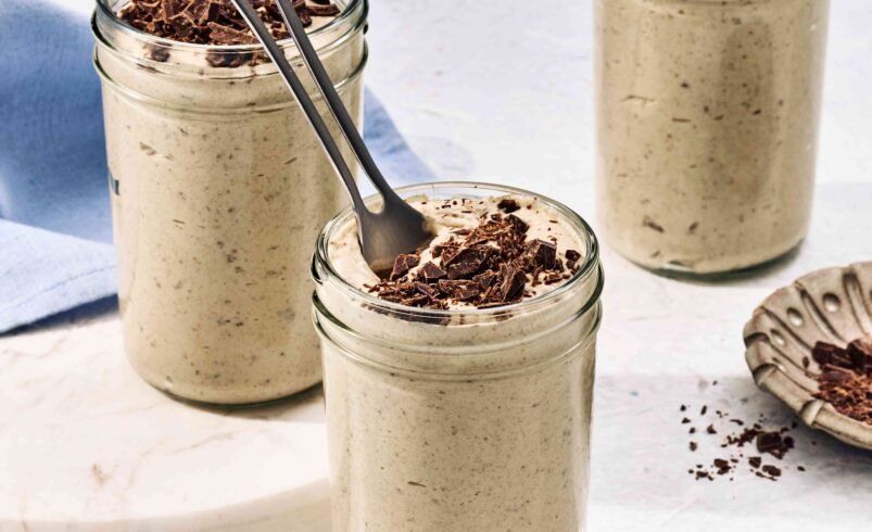 Três potes de vidro com creme doce coberto por lascas de chocolate e colher.