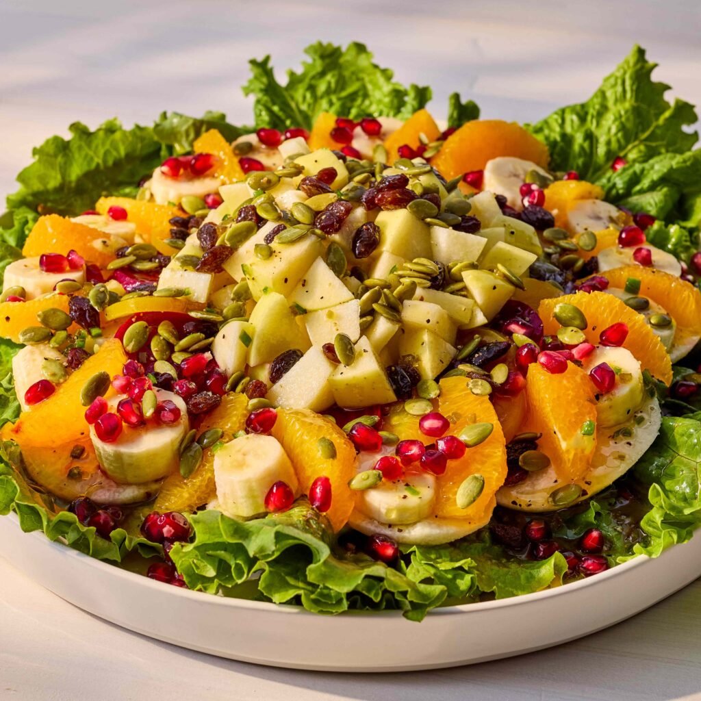 Salada colorida com frutas sortidas, folhas verdes, sementes e uvas-passas.