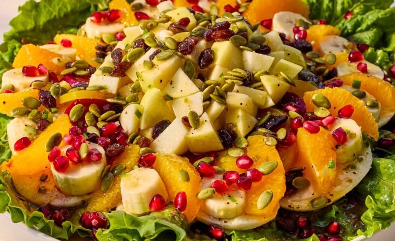 Salada colorida com frutas sortidas, folhas verdes, sementes e uvas-passas.
