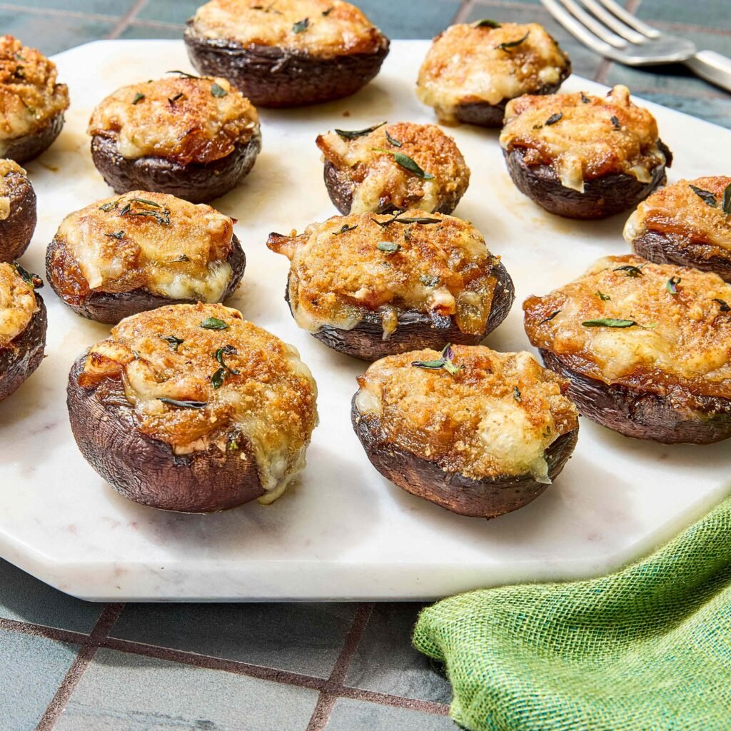 Cogumelos recheados assados com queijo e ervas em prato de mármore branco.