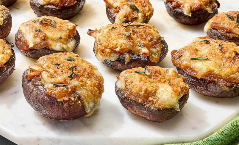 Cogumelos recheados assados com queijo e ervas em prato de mármore branco.