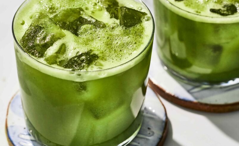 Duas bebidas verdes com gelo servidas em copos de vidro sobre porta-copos.