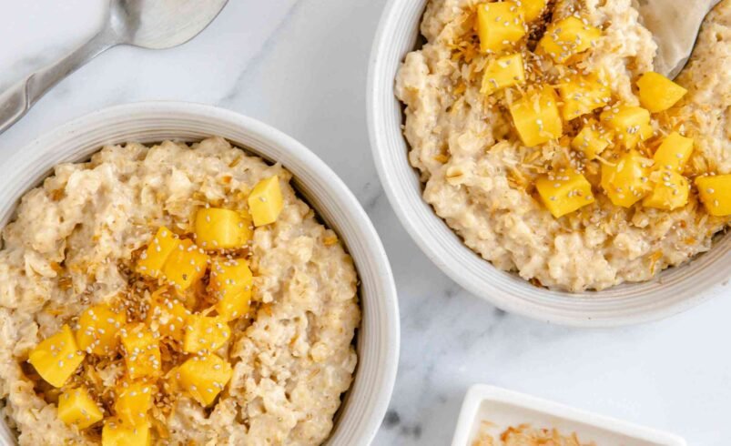 Duas tigelas de aveia cremosa decorada com pedaços de manga e coco tostado.
