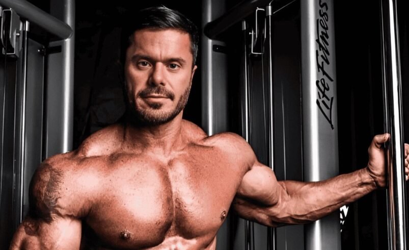 Homem musculoso levantando peso em equipamento de academia, evidenciando o peitoral.