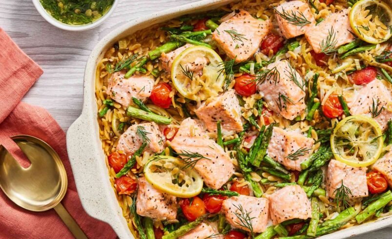 Travessa com pedaços de salmão, arroz, tomates, aspargos e limão.