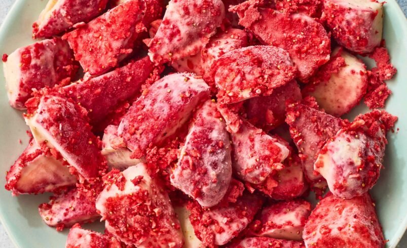 Morangos com cobertura de chocolate branco e pedaços de crumble vermelho em prato verde.