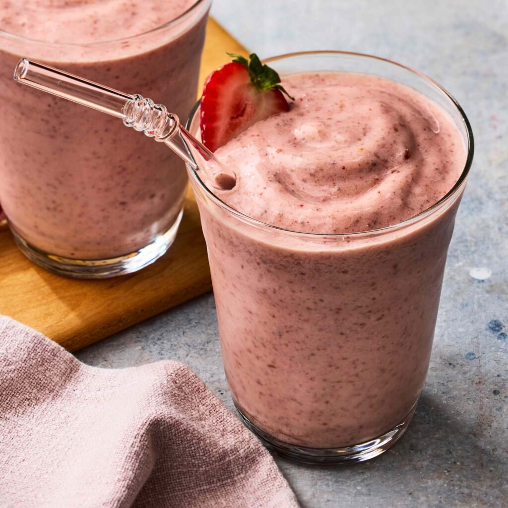 Copos de smoothie de morango cremoso com morango decorativo e canudo transparente.