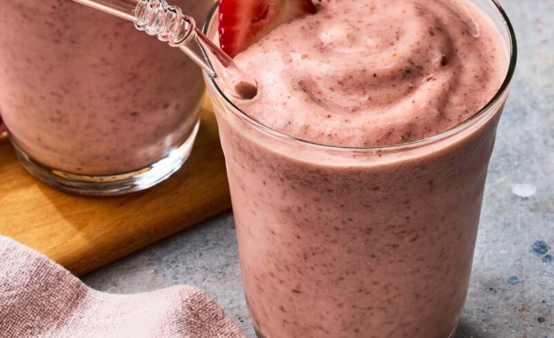 Copos de smoothie de morango cremoso com morango decorativo e canudo transparente.