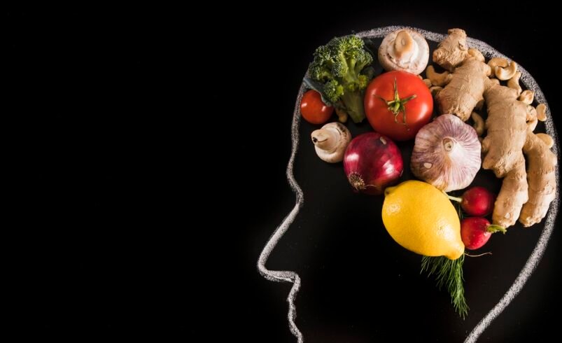 Silhueta de cabeça feita com vegetais como tomate, brócolis e gengibre.
