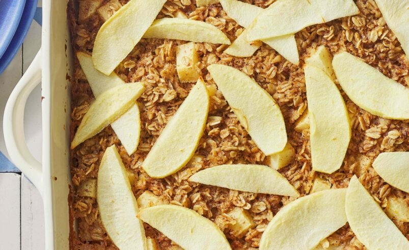 Travessa com assado de maçã e cobertura de aveia em uma superfície azul e branca.