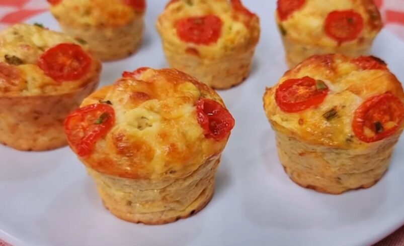 Seis muffins salgados com tomate e queijo sobre um prato branco.
