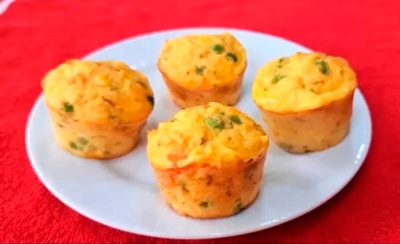 Quatro muffins salgados com vegetais sobre um prato branco em toalha vermelha.