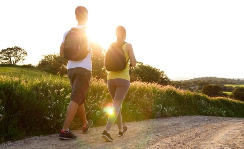 Casal caminhando em trilha ao ar livre com sol ao fundo.