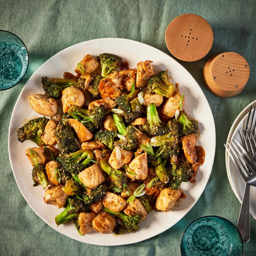 Prato de frango com brócolis grelhados servido em uma mesa verde.