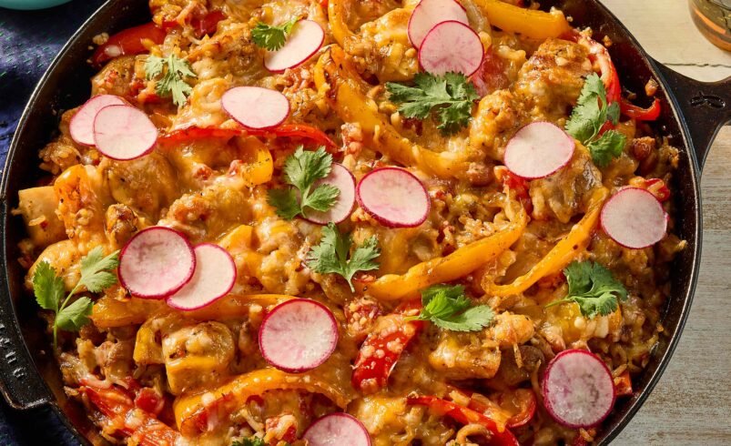 Prato colorido em frigideira com legumes, queijo derretido e rabanetes fatiados.