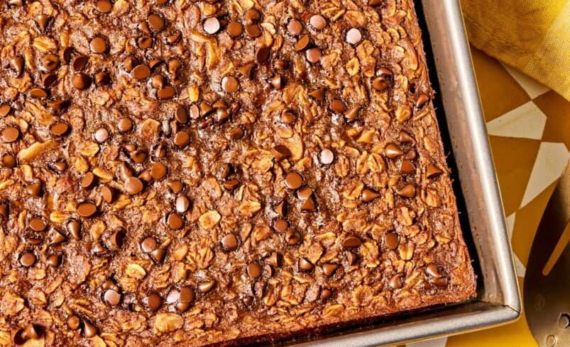 Bolo de chocolate com gotas de chocolate em uma assadeira retangular, com fundo amarelo.